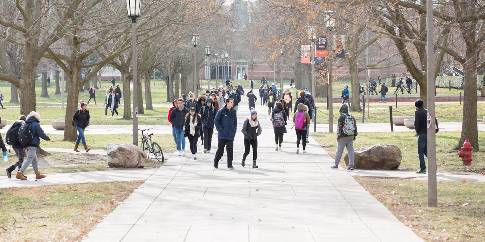 Students walking to class on the sidewalk south of Gregory Hall looking towards Temple Hoyne Buell Hall.